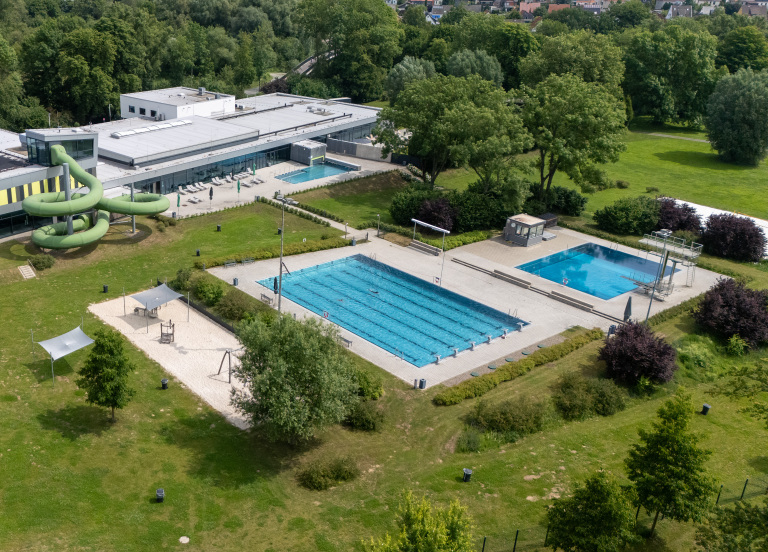Ein Bild aus der Vogelperspektive. Man sieht ein Schwimmer- udn ein Sprungbecken, und eine Röhrenrutsche, in mitten von grüner Landschaft.